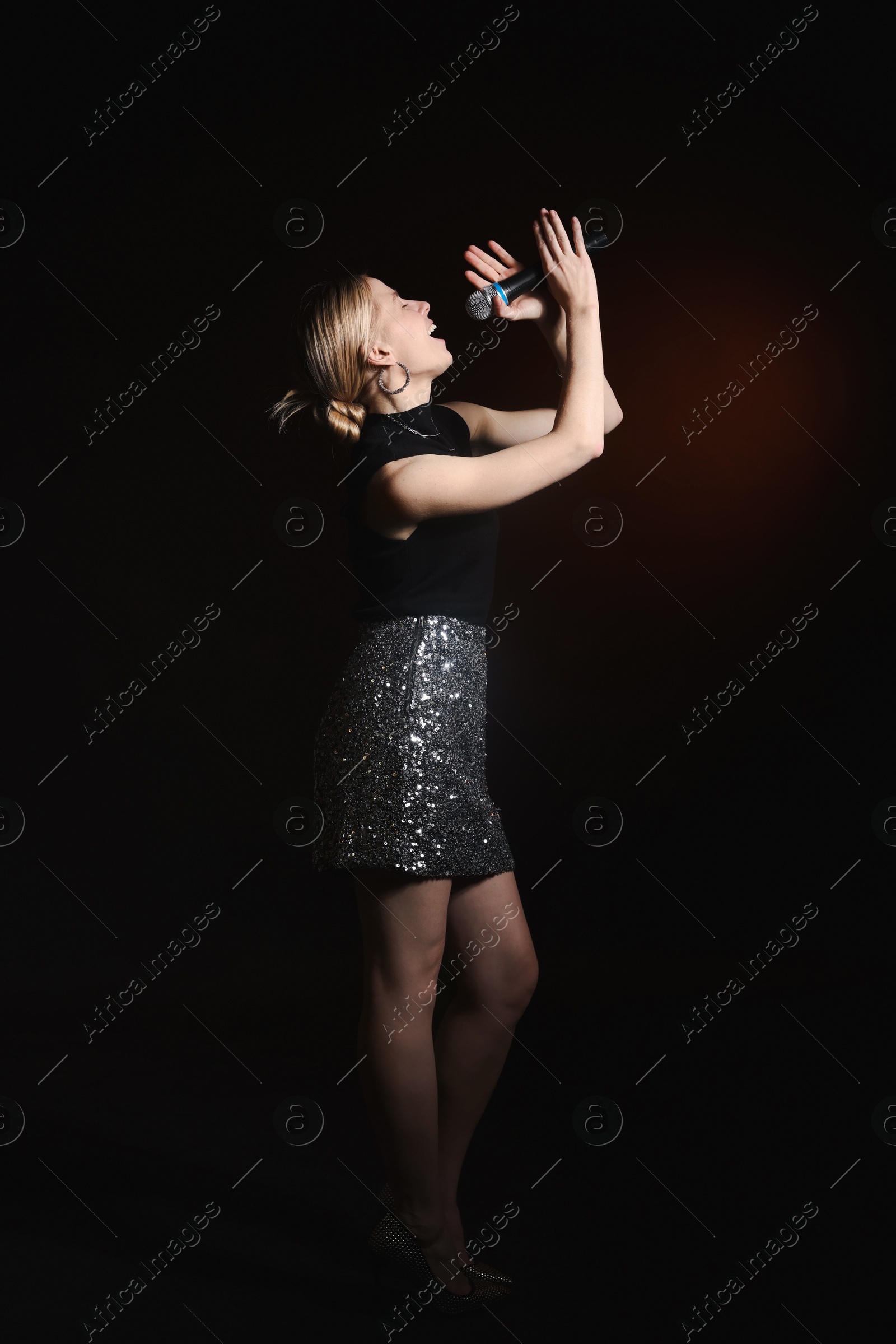 Photo of Beautiful singer performing on dark background with color light