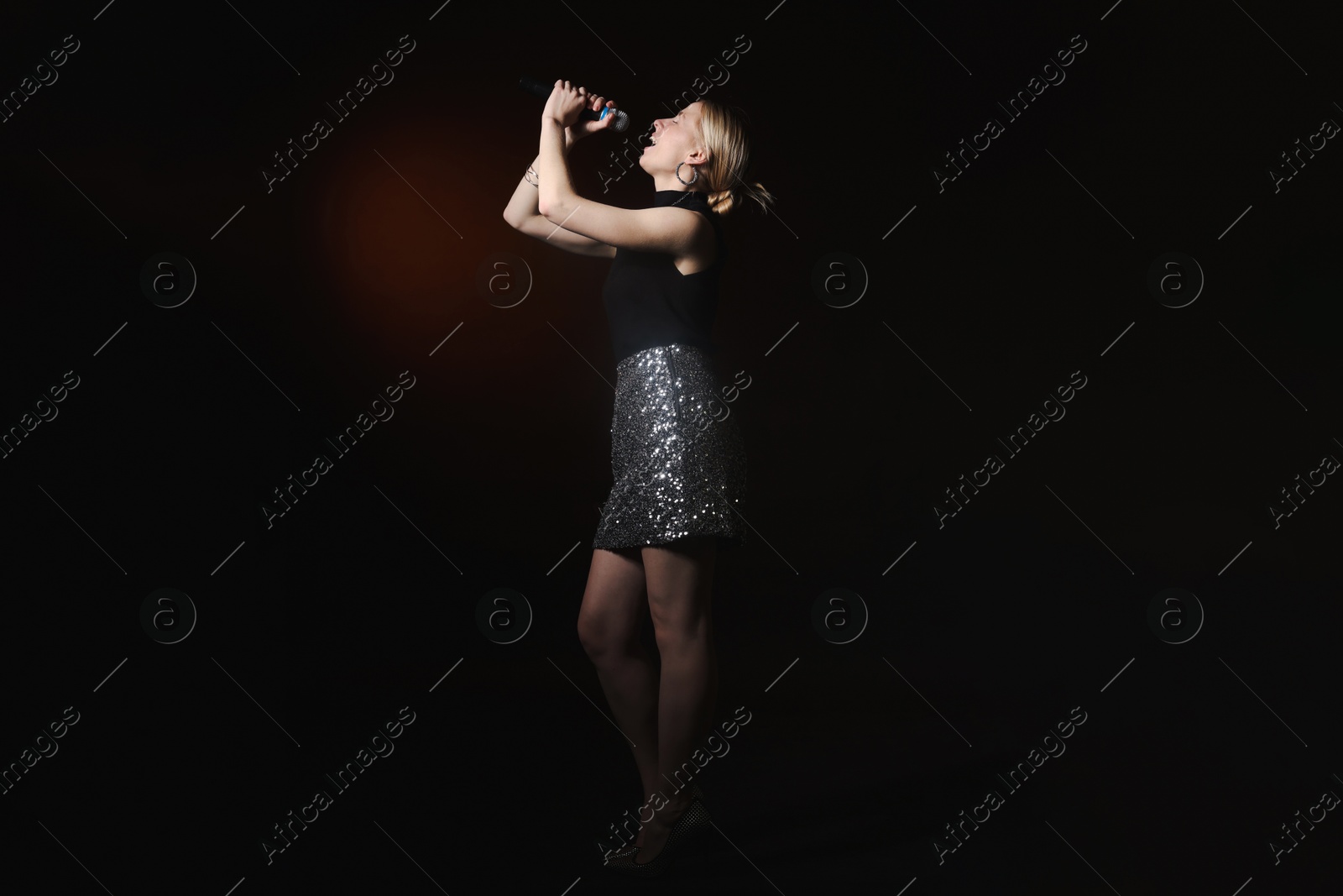 Photo of Beautiful singer performing on dark background with color light