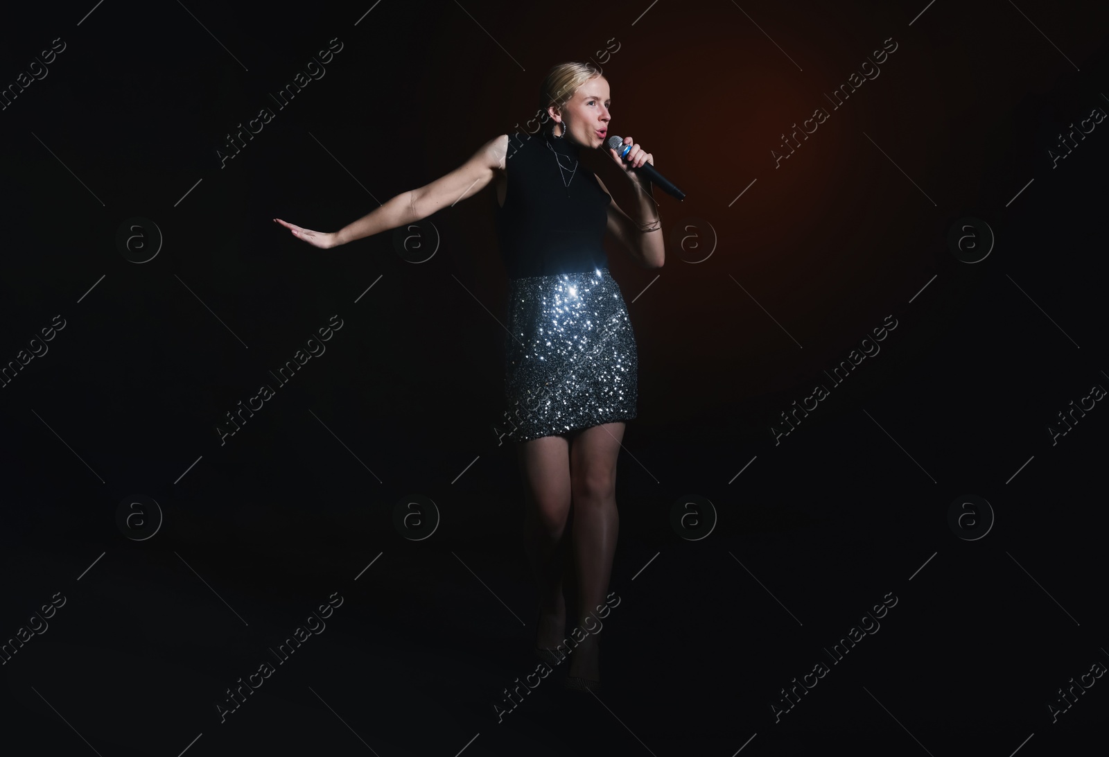 Photo of Beautiful singer performing on dark background with color light