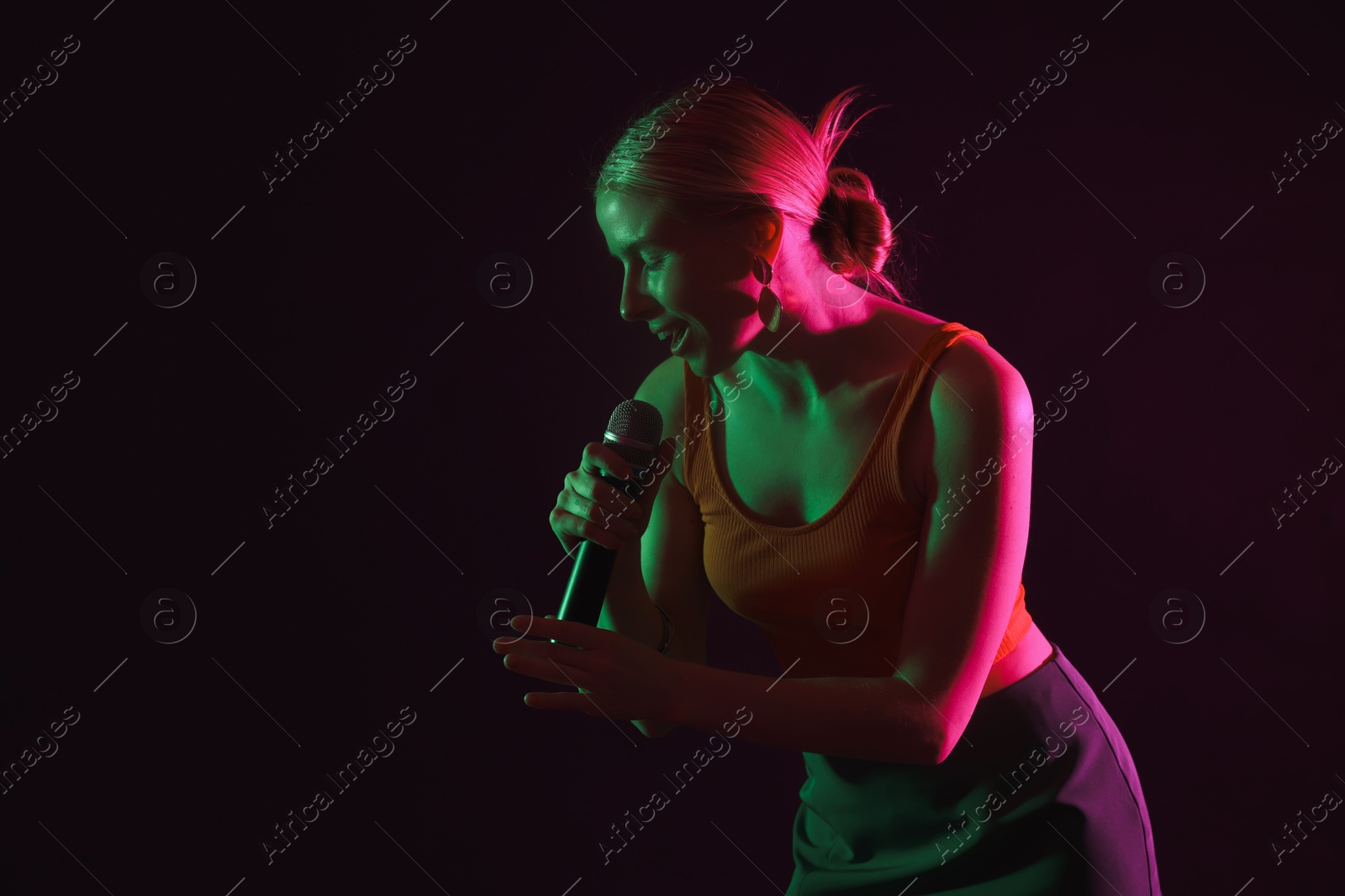 Photo of Beautiful singer performing on dark background in color lights. Space for text