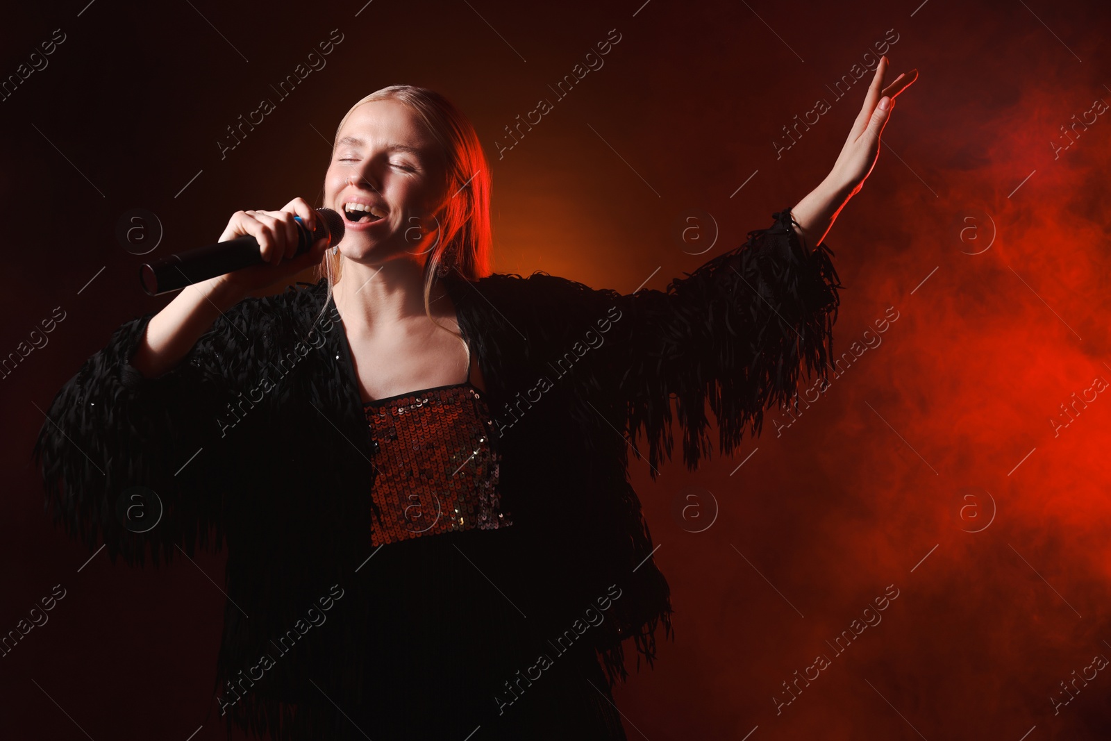 Photo of Beautiful singer performing on dark background with red light and smoke