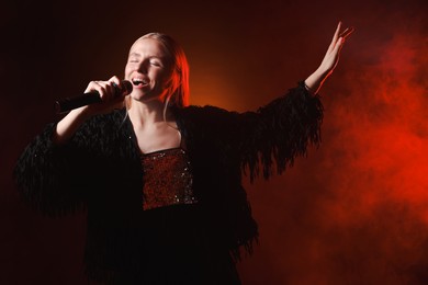 Photo of Beautiful singer performing on dark background with red light and smoke