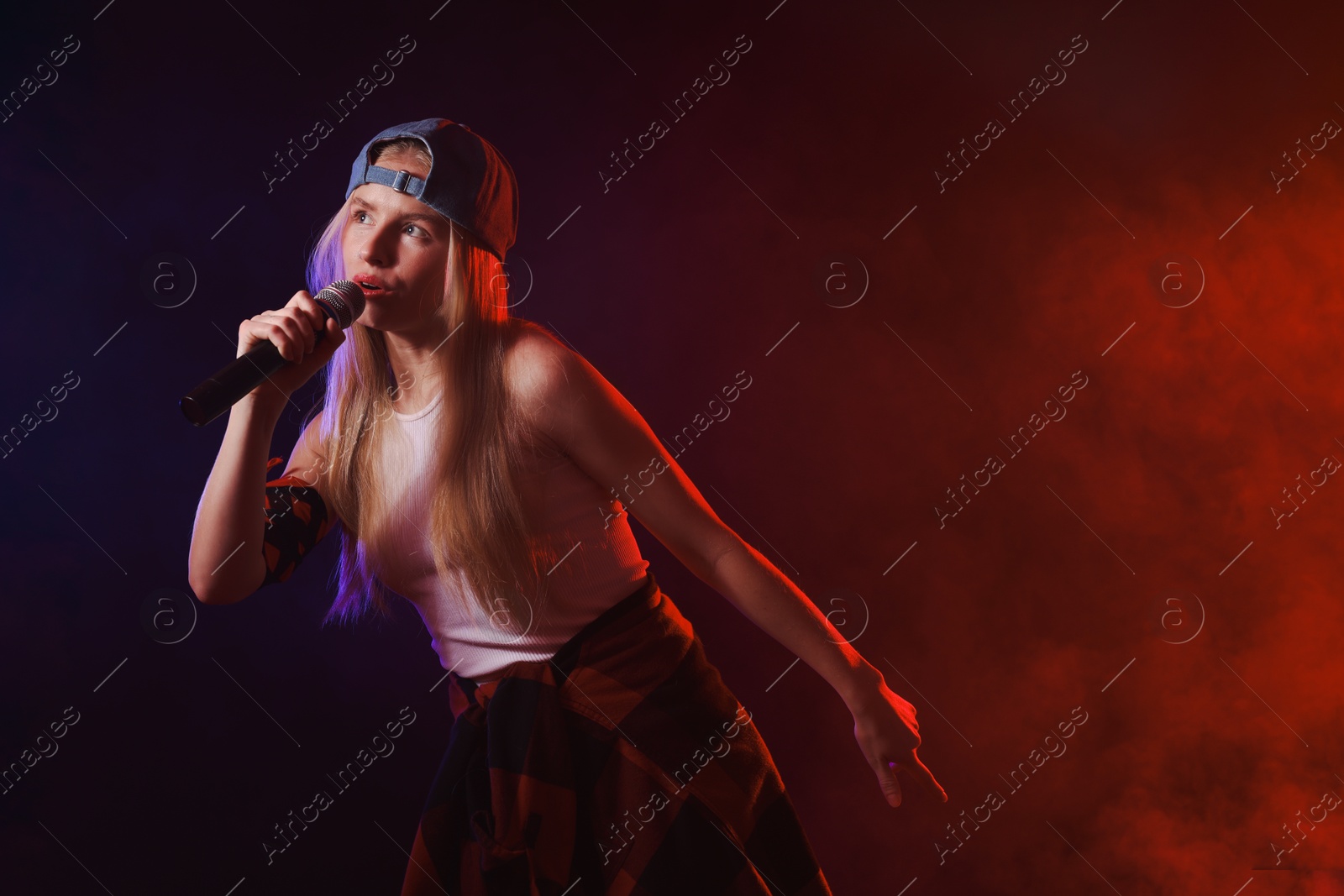 Photo of Talented singer performing on dark background with color lights and smoke. Space for text