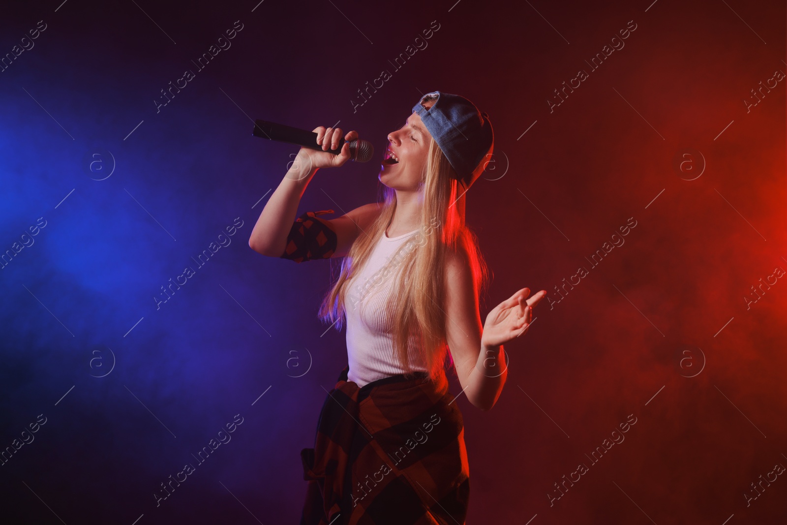 Photo of Talented singer performing on dark background with color lights and smoke