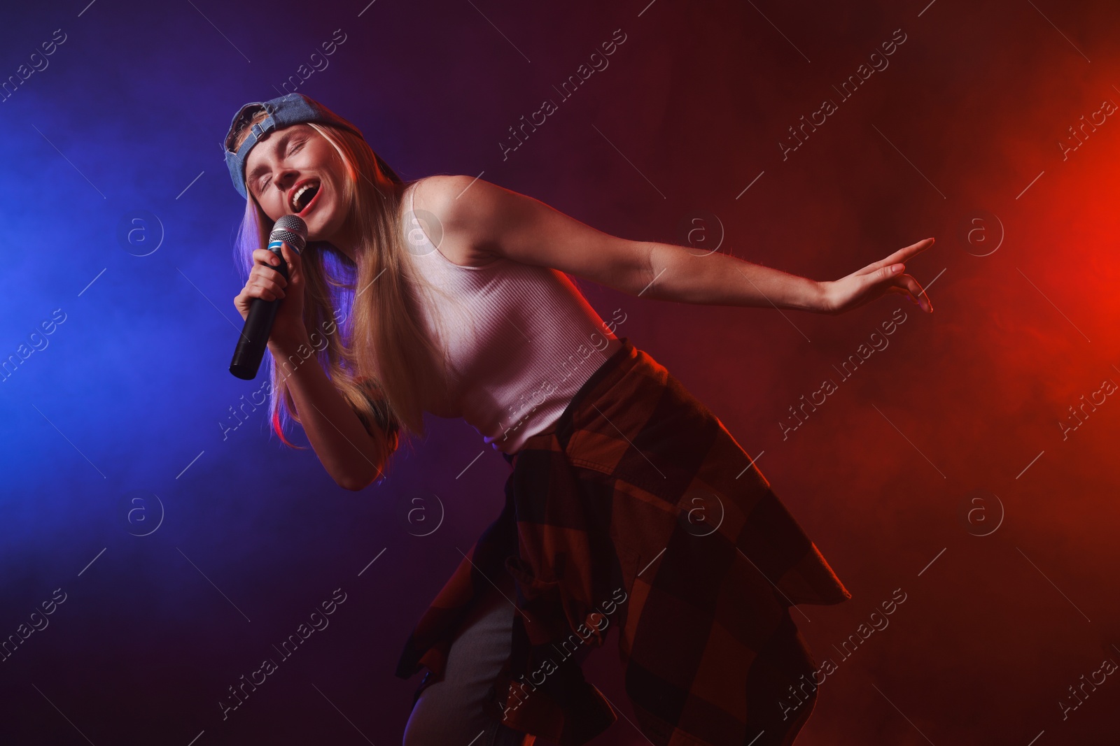 Photo of Talented singer performing on dark background with color lights and smoke