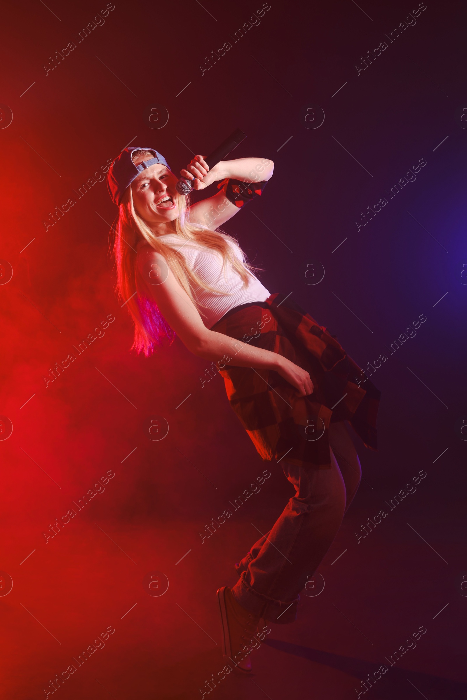 Photo of Talented singer performing on dark background with color lights and smoke