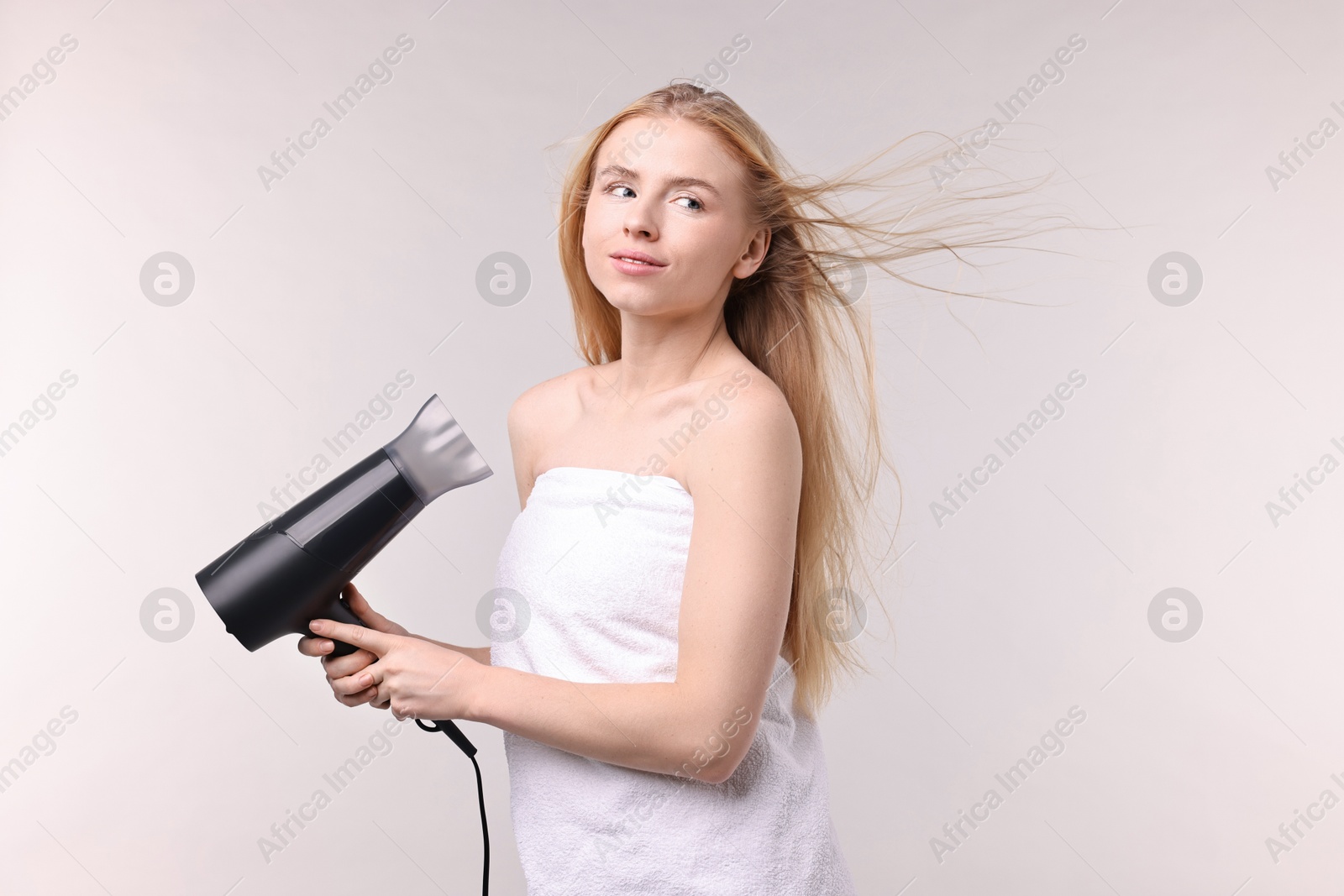 Photo of Beautiful young woman drying her hair with hairdryer on light grey background