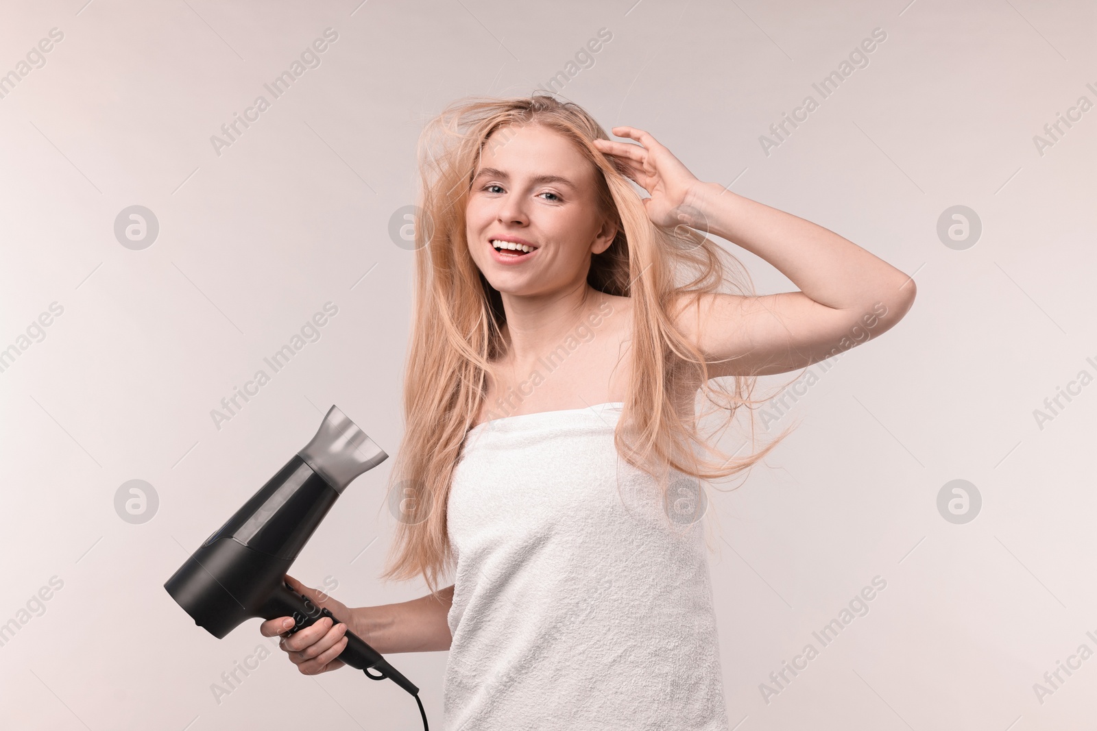 Photo of Beautiful young woman drying her hair with hairdryer on light grey background