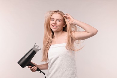 Beautiful young woman drying her hair with hairdryer on light grey background