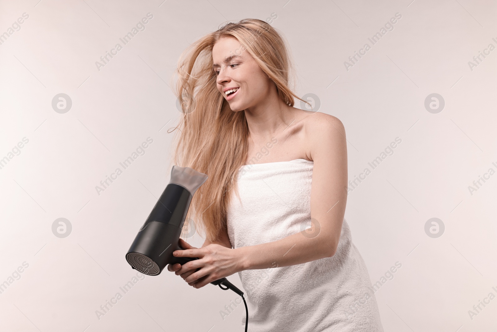 Photo of Beautiful young woman drying her hair with hairdryer on light grey background