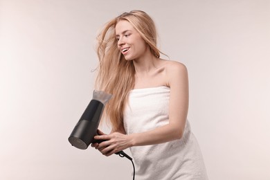 Photo of Beautiful young woman drying her hair with hairdryer on light grey background