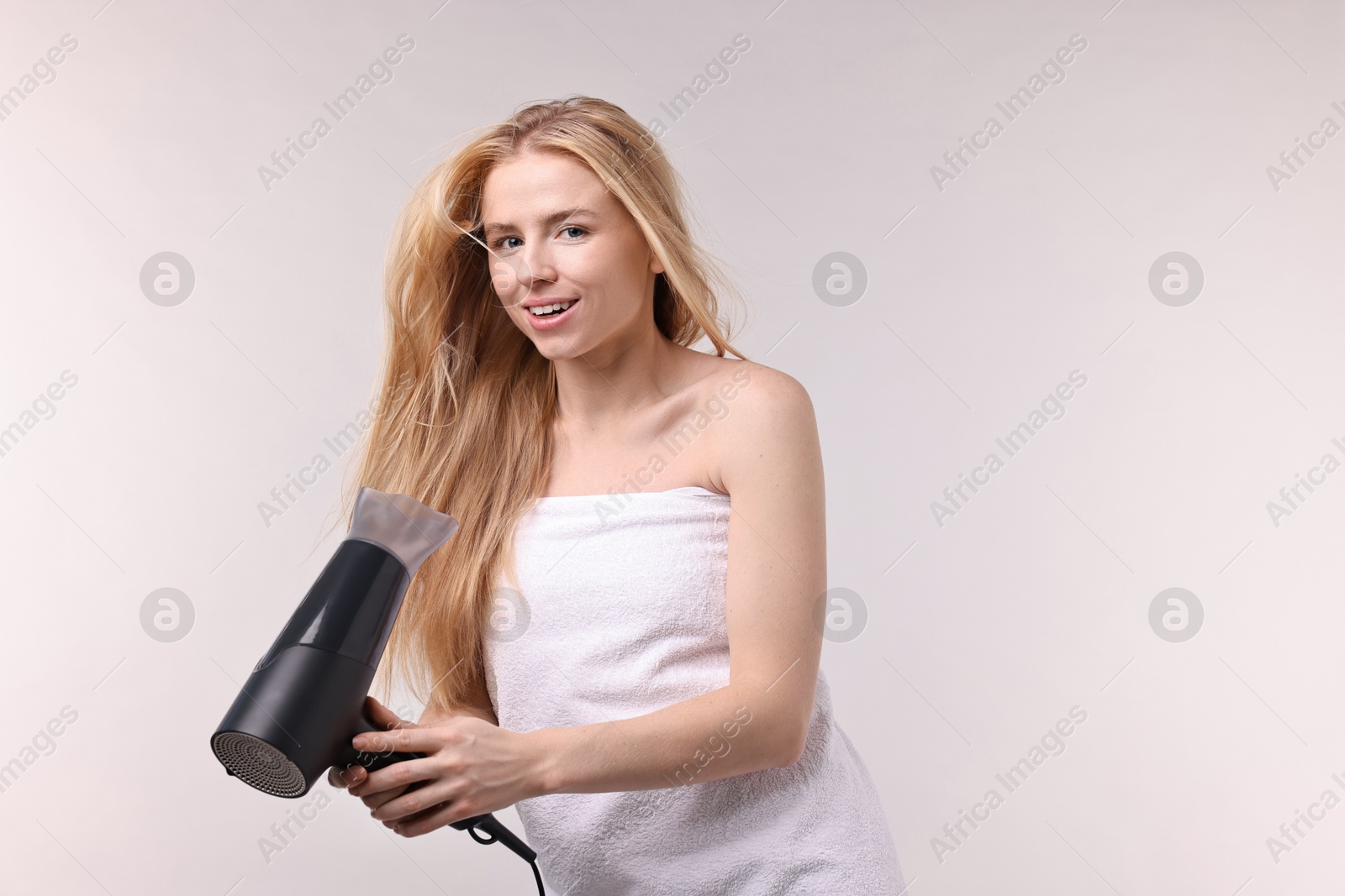 Photo of Beautiful young woman drying her hair with hairdryer on light grey background