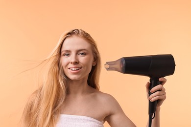 Photo of Beautiful young woman drying her hair with hairdryer on beige background