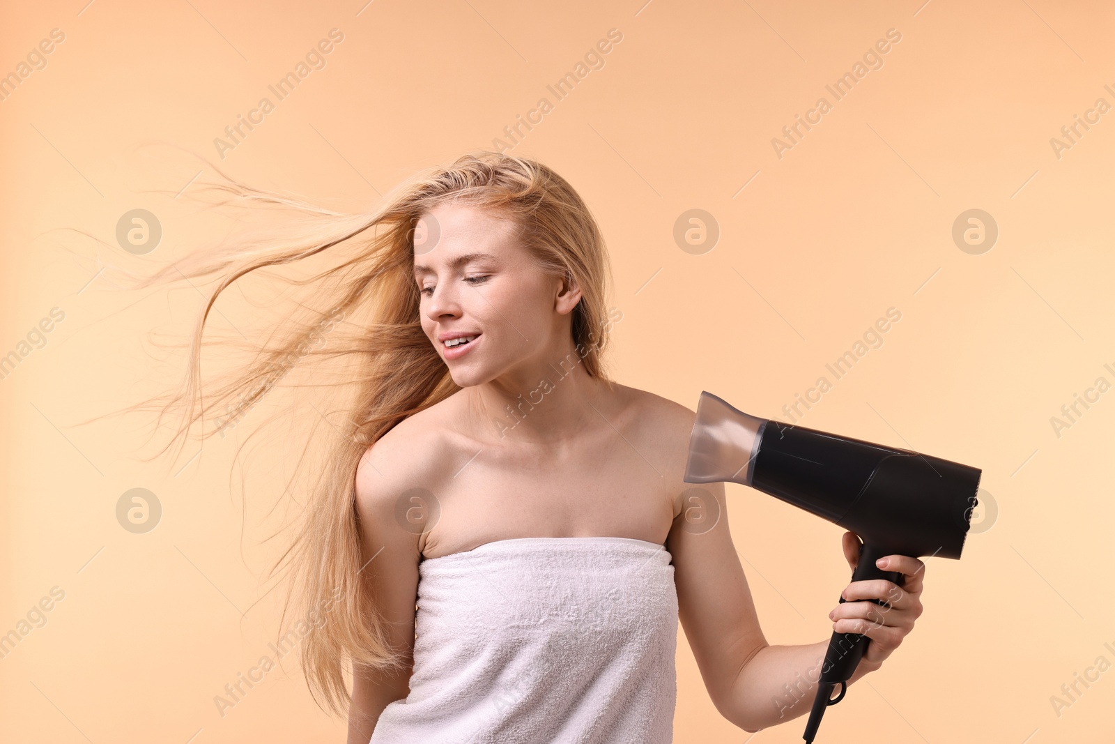 Photo of Beautiful young woman drying her hair with hairdryer on beige background