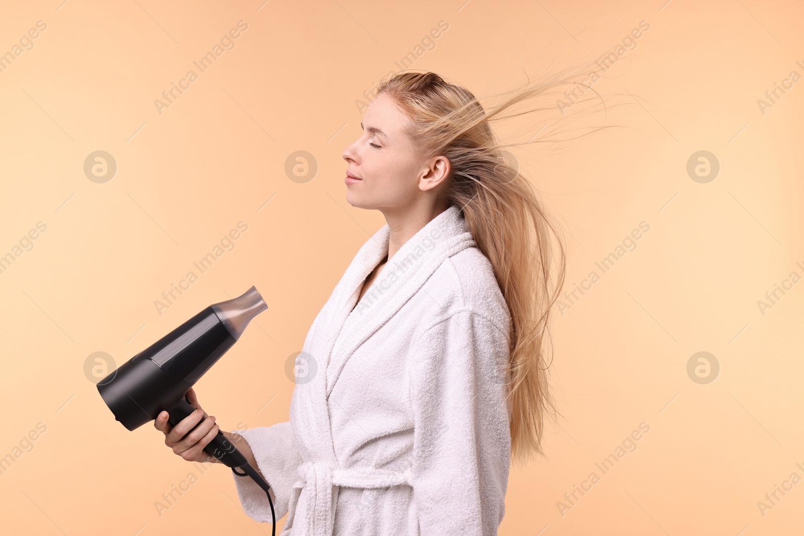 Photo of Beautiful young woman drying her hair with hairdryer on beige background