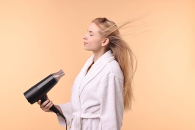 Beautiful young woman drying her hair with hairdryer on beige background