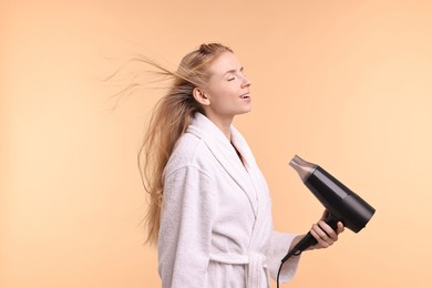 Beautiful young woman drying her hair with hairdryer on beige background