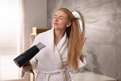 Beautiful young woman drying her hair in bathroom