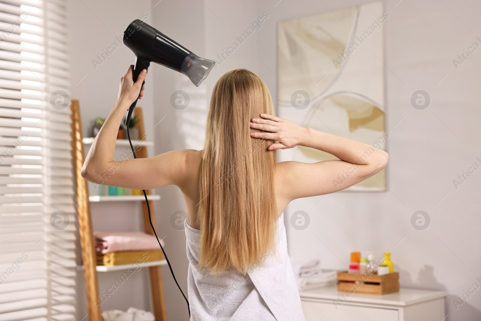 Photo of Beautiful young woman drying her hair in bathroom, back view