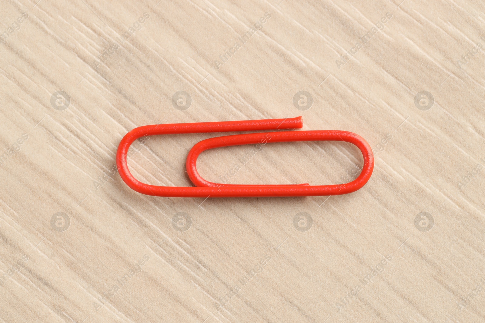 Photo of One red paper clip on wooden table, top view