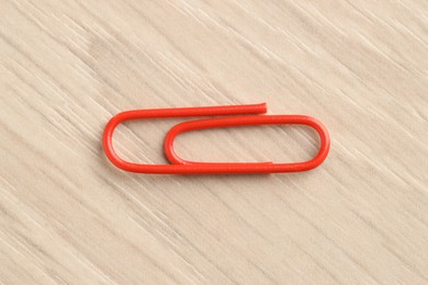 Photo of One red paper clip on wooden table, top view