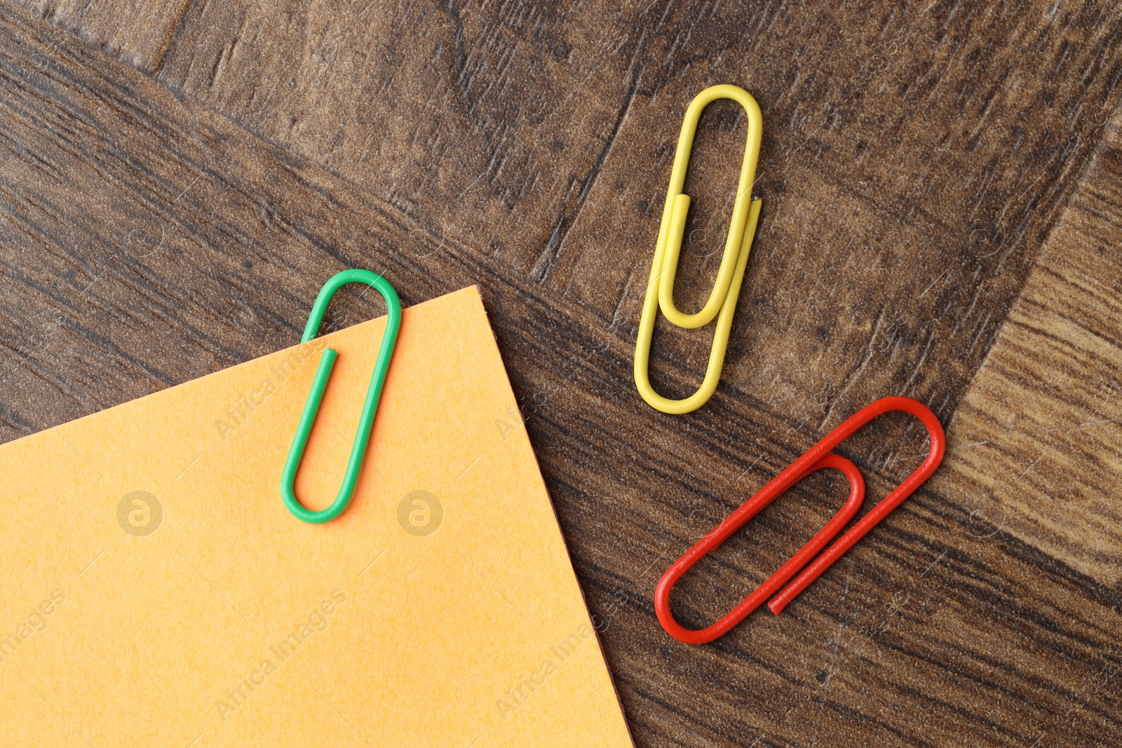 Photo of Paper note and many colorful clips on wooden table, flat lay