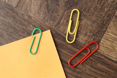 Photo of Paper note and many colorful clips on wooden table, flat lay