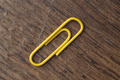 Photo of One yellow paper clip on wooden table, top view