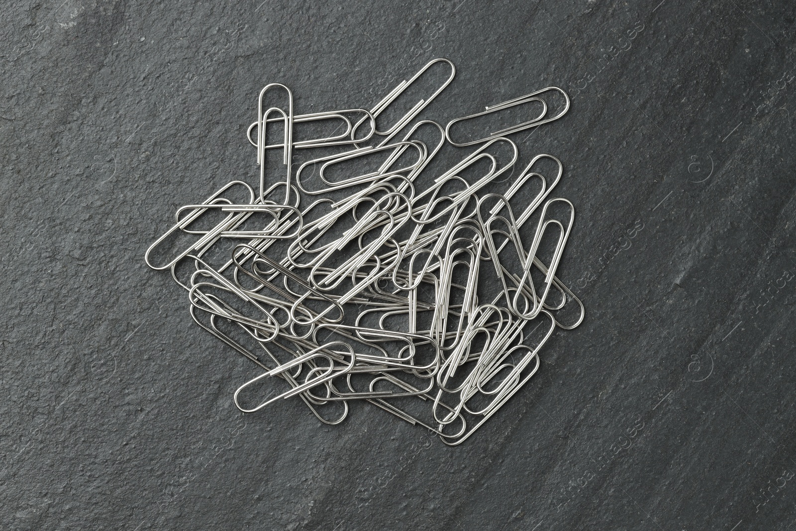 Photo of Many metal paper clips on black table, top view.