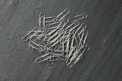 Photo of Many metal paper clips on black table, top view.