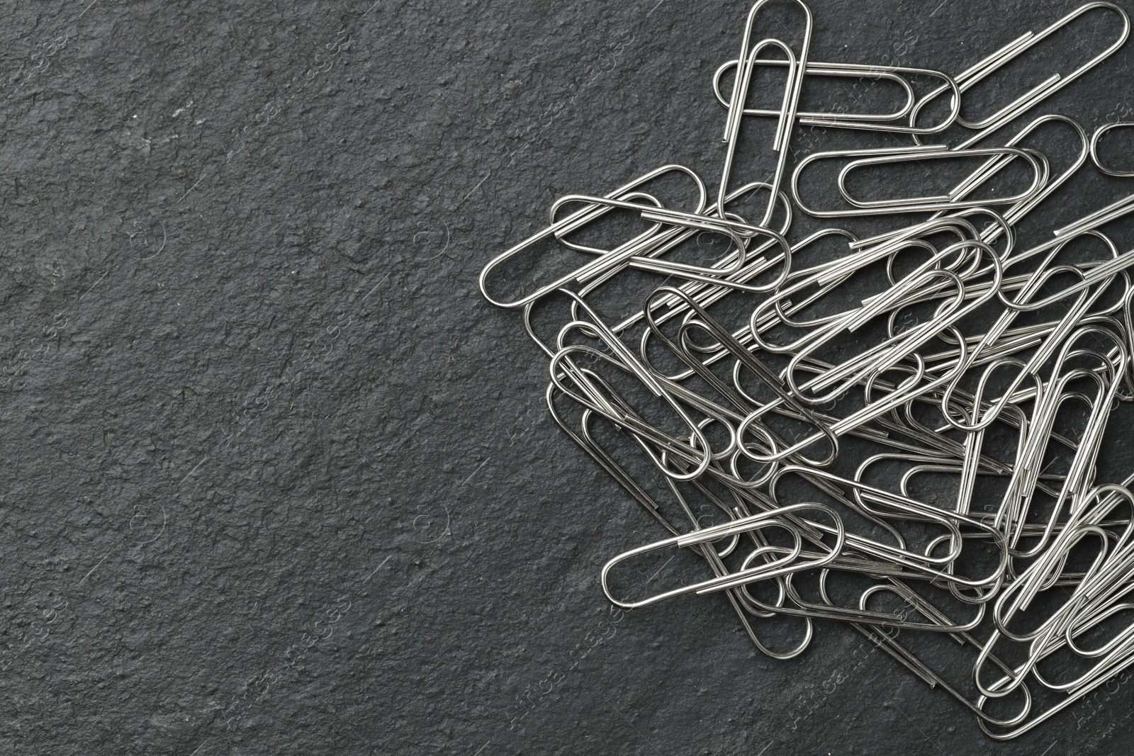 Photo of Many metal paper clips on black table, top view. Space for text