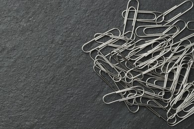 Photo of Many metal paper clips on black table, top view. Space for text