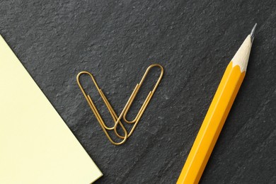 Photo of Paper notes, pencil and clips on black table, flat lay