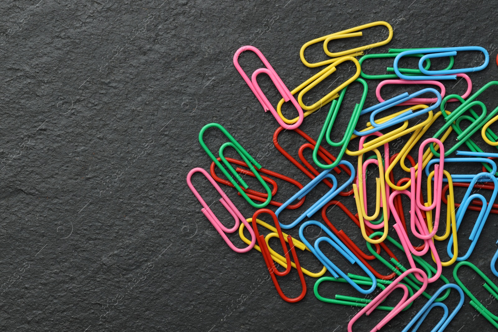 Photo of Many colorful paper clips on black table, top view. Space for text