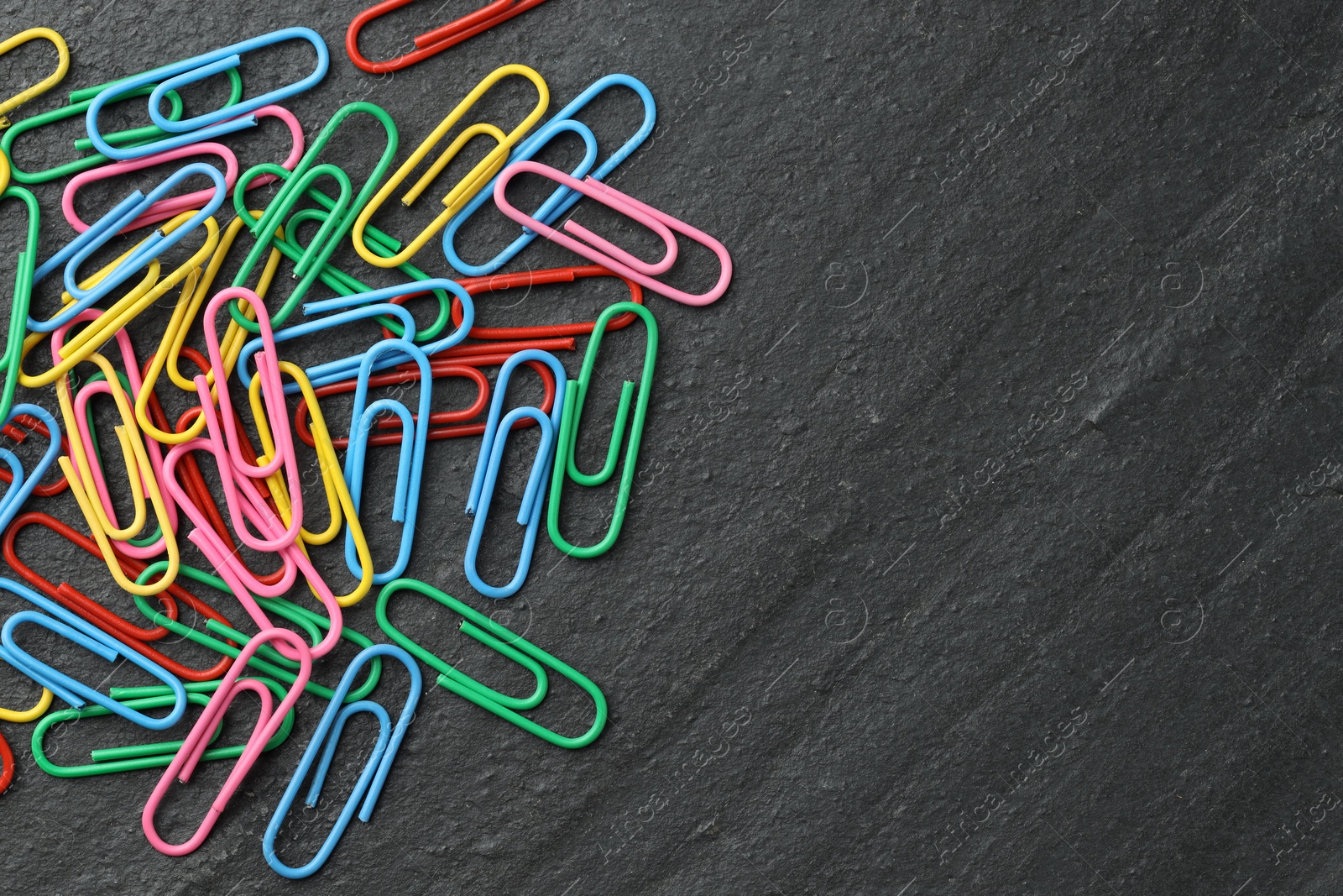 Photo of Many colorful paper clips on black table, top view. Space for text