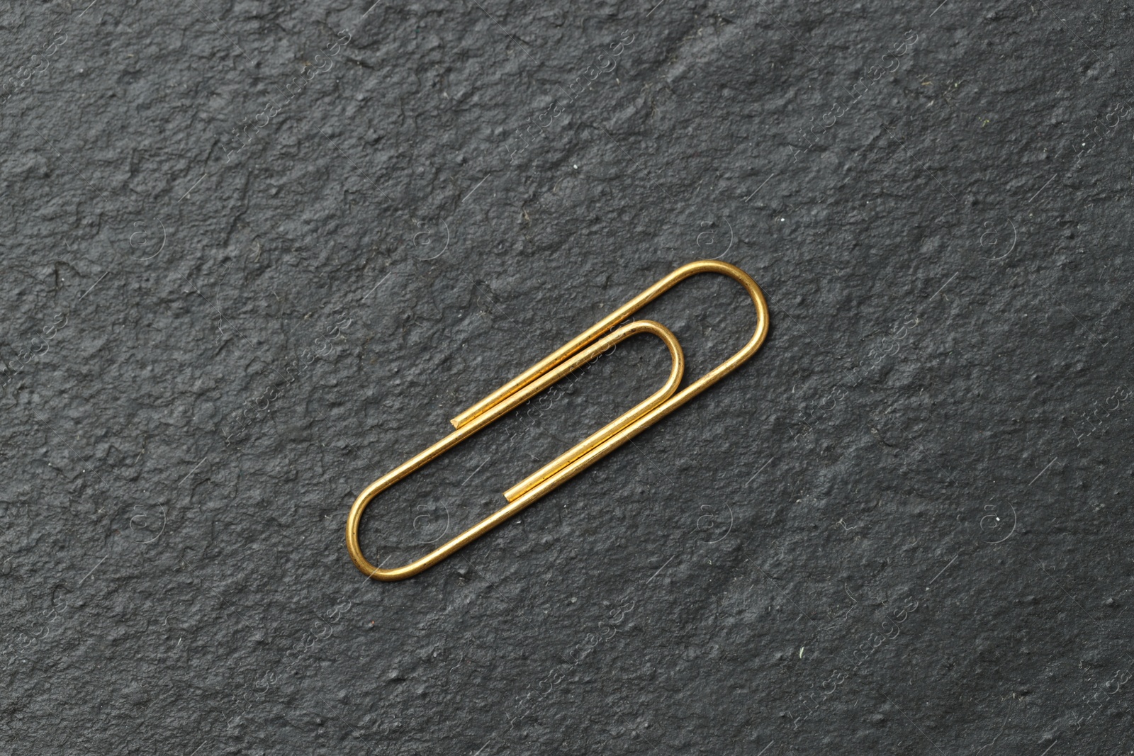 Photo of One golden paper clip on black table, top view