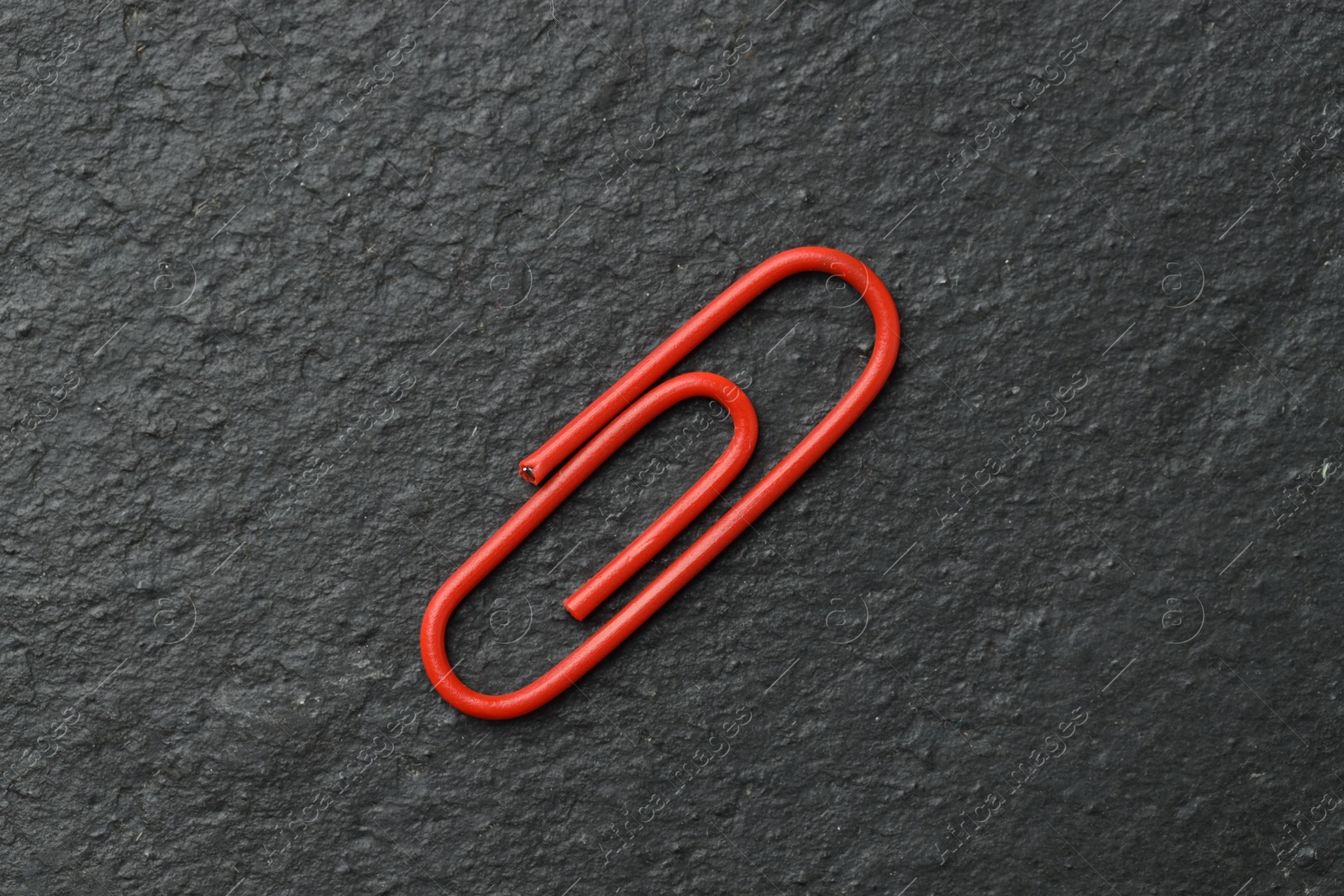 Photo of One red paper clip on black table, top view