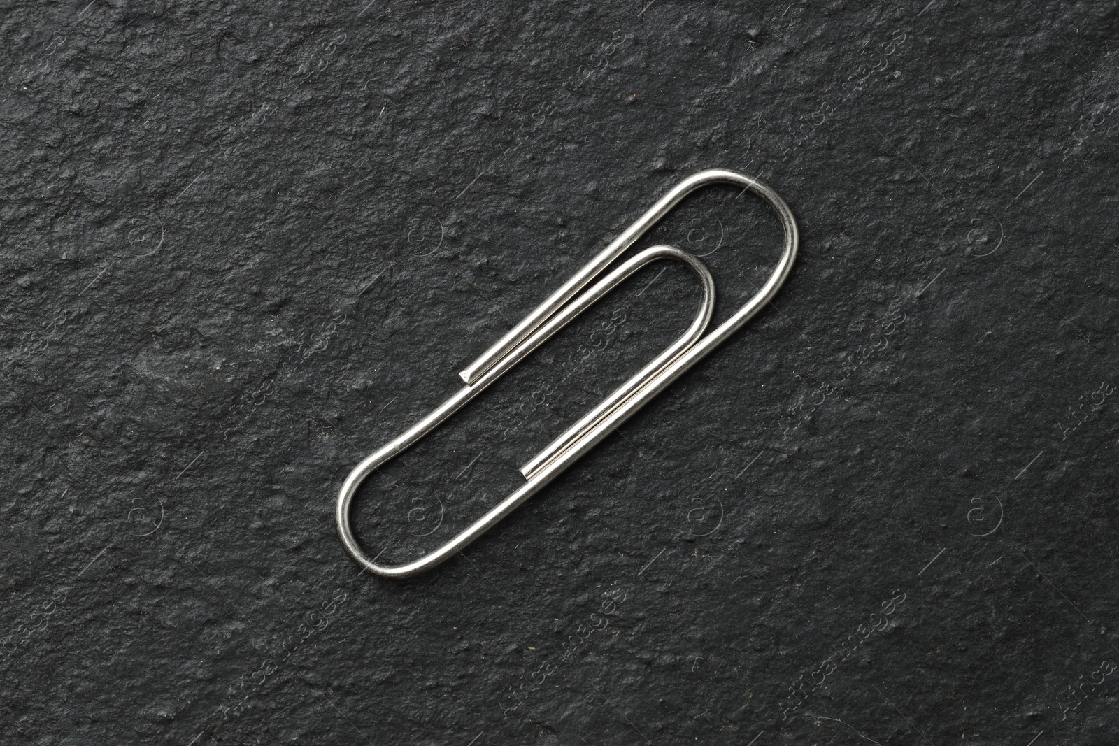 Photo of One metal paper clip on black table, top view