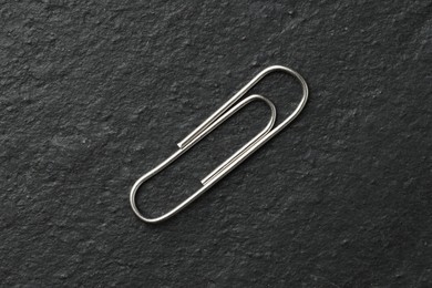 Photo of One metal paper clip on black table, top view