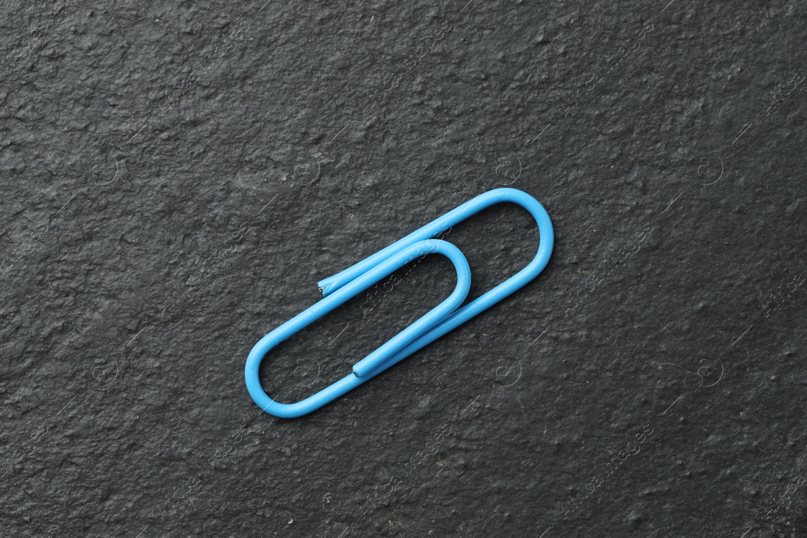 Photo of One blue paper clip on black table, top view