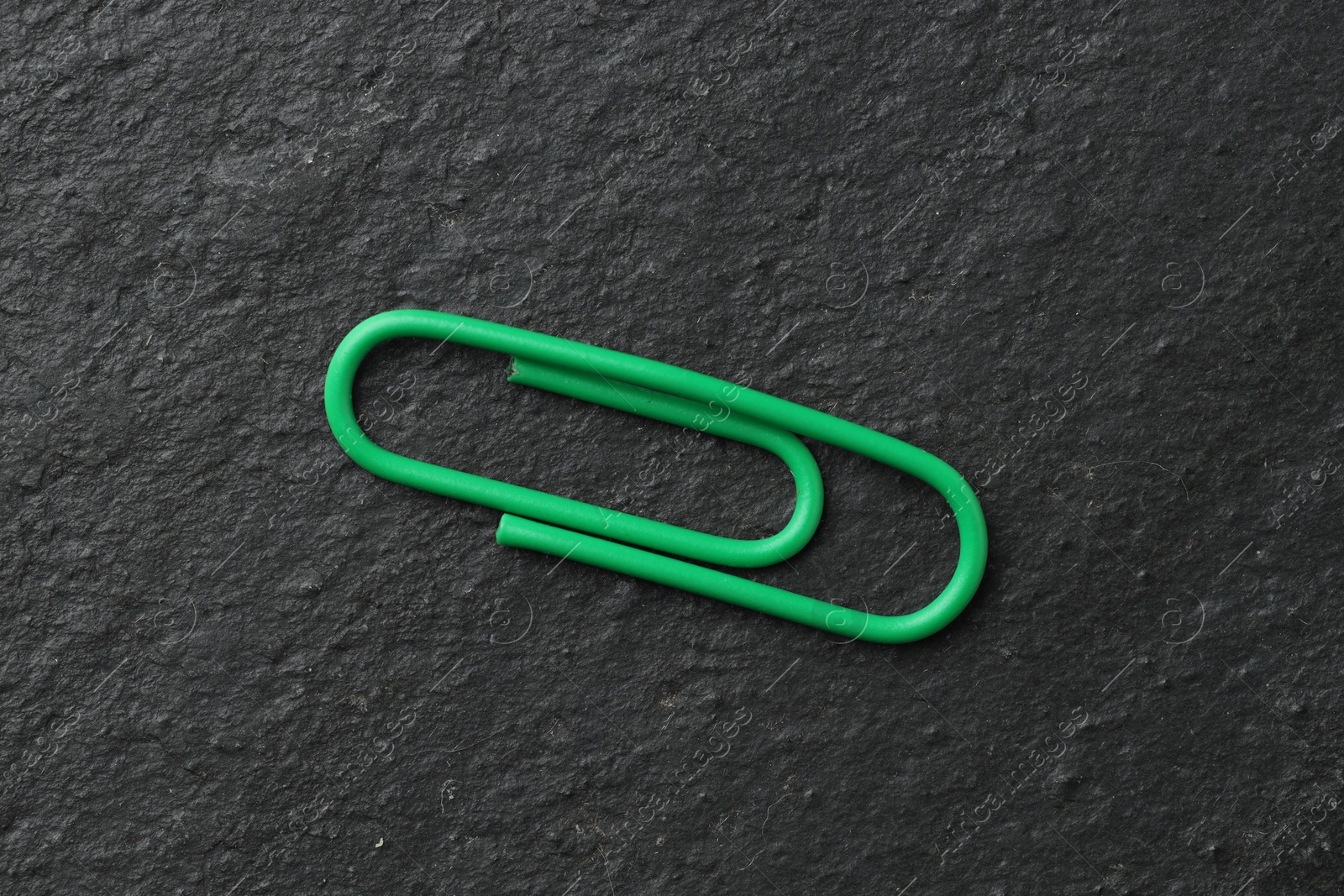 Photo of One green paper clip on black table, top view