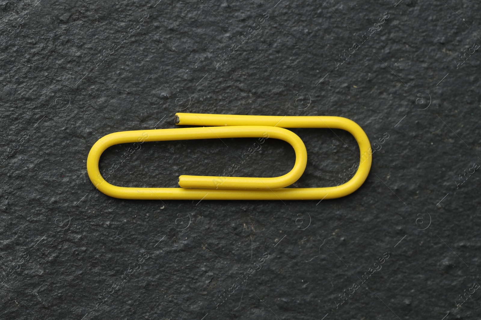 Photo of One yellow paper clip on black table, top view