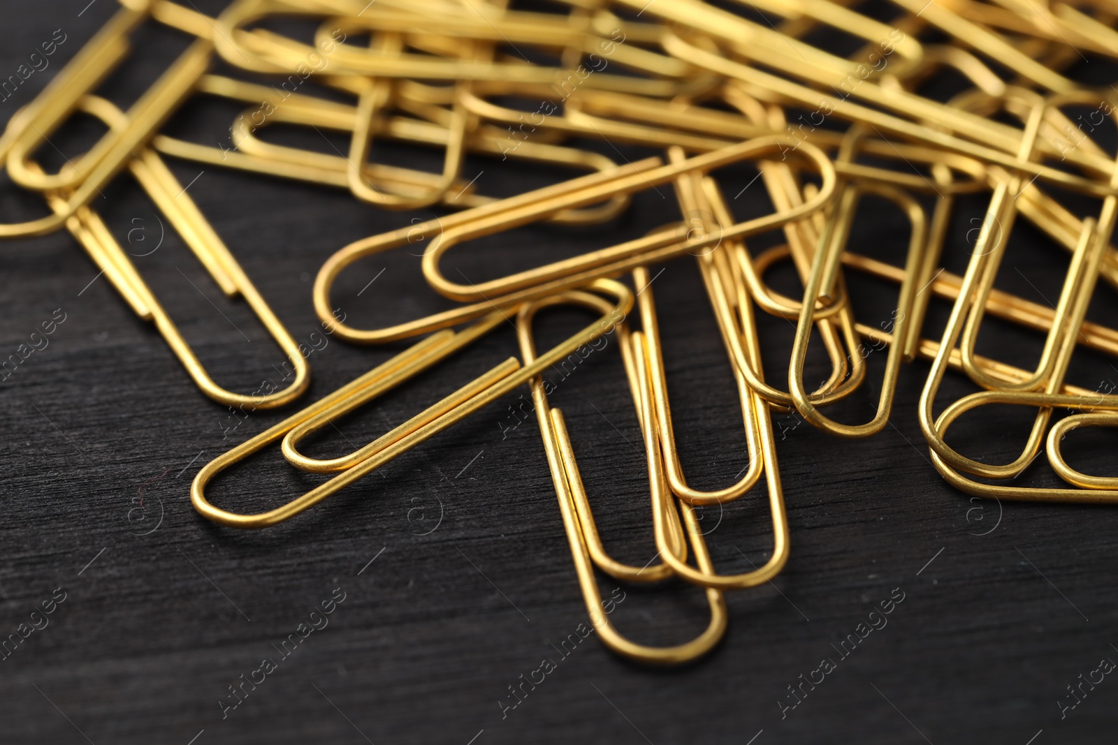 Photo of Many golden paper clips on black table, closeup