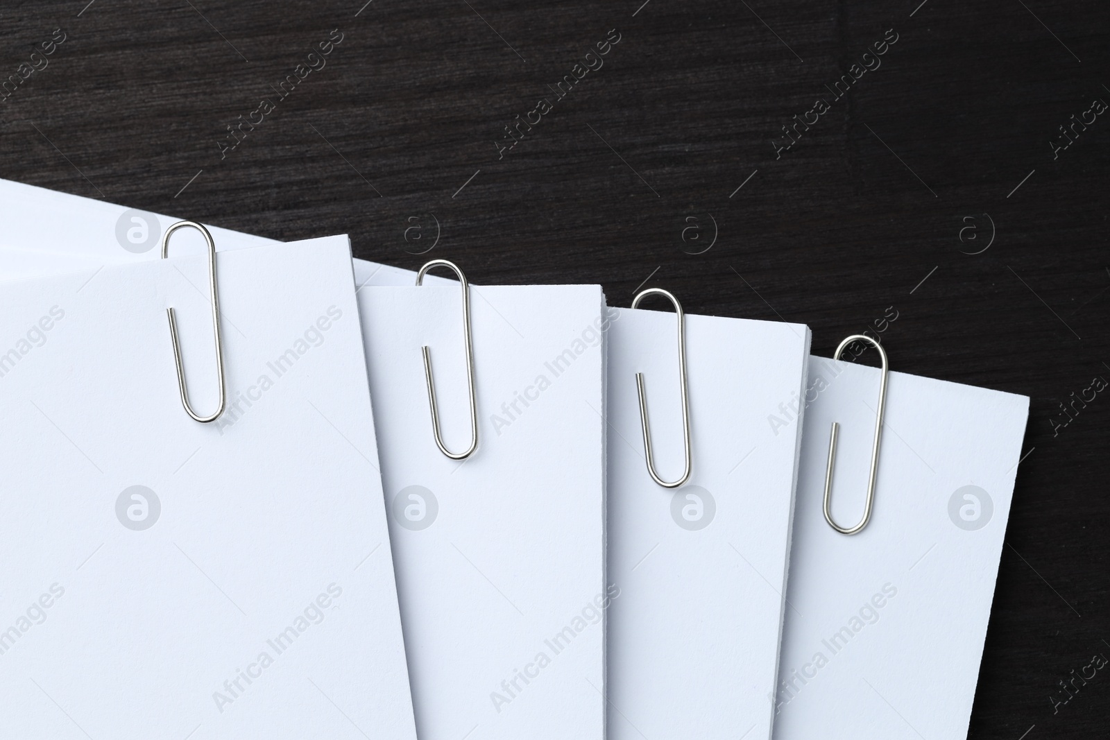 Photo of Paper notes with metal clips on black wooden table, top view