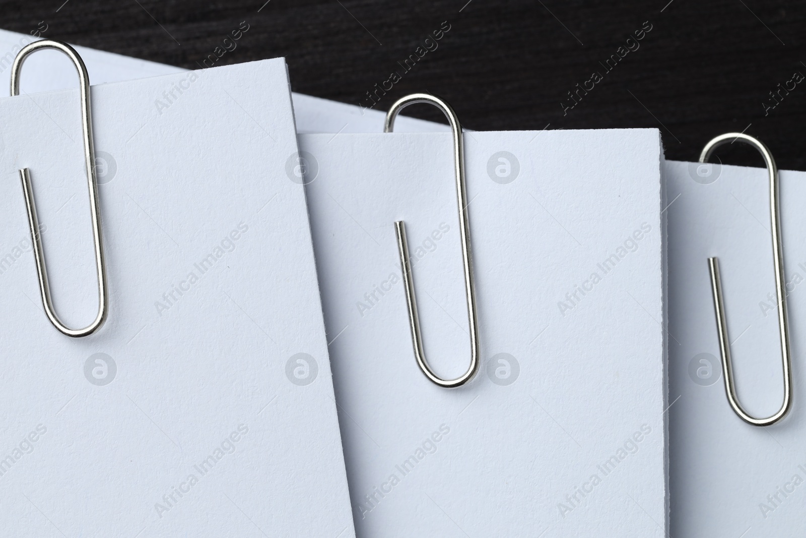 Photo of Paper notes with metal clips on black wooden table, top view