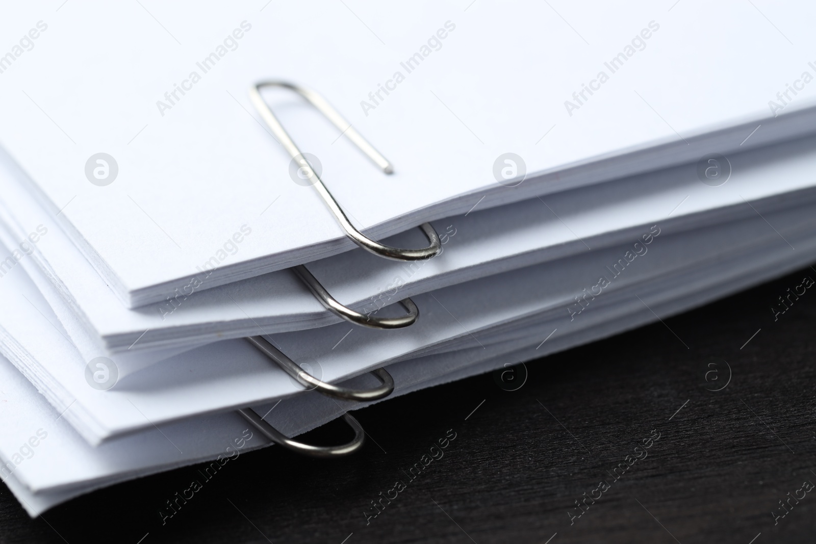 Photo of Paper notes with metal clips on black wooden table, closeup