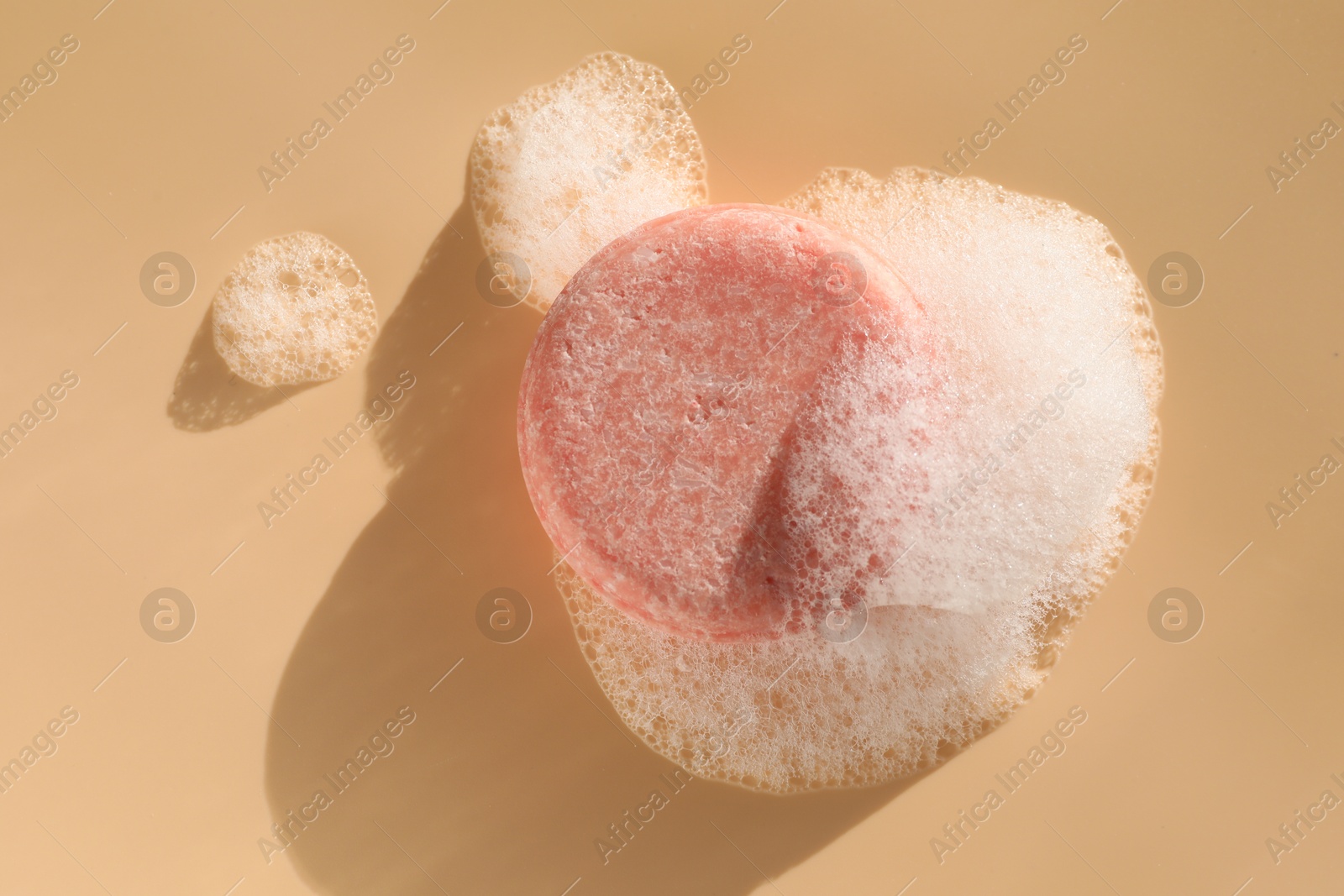 Photo of Soap bar with foam on peach background, top view