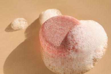 Photo of Soap bar with foam on peach background, closeup