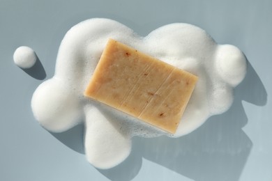 Photo of Soap bar with foam on grayish blue background, top view