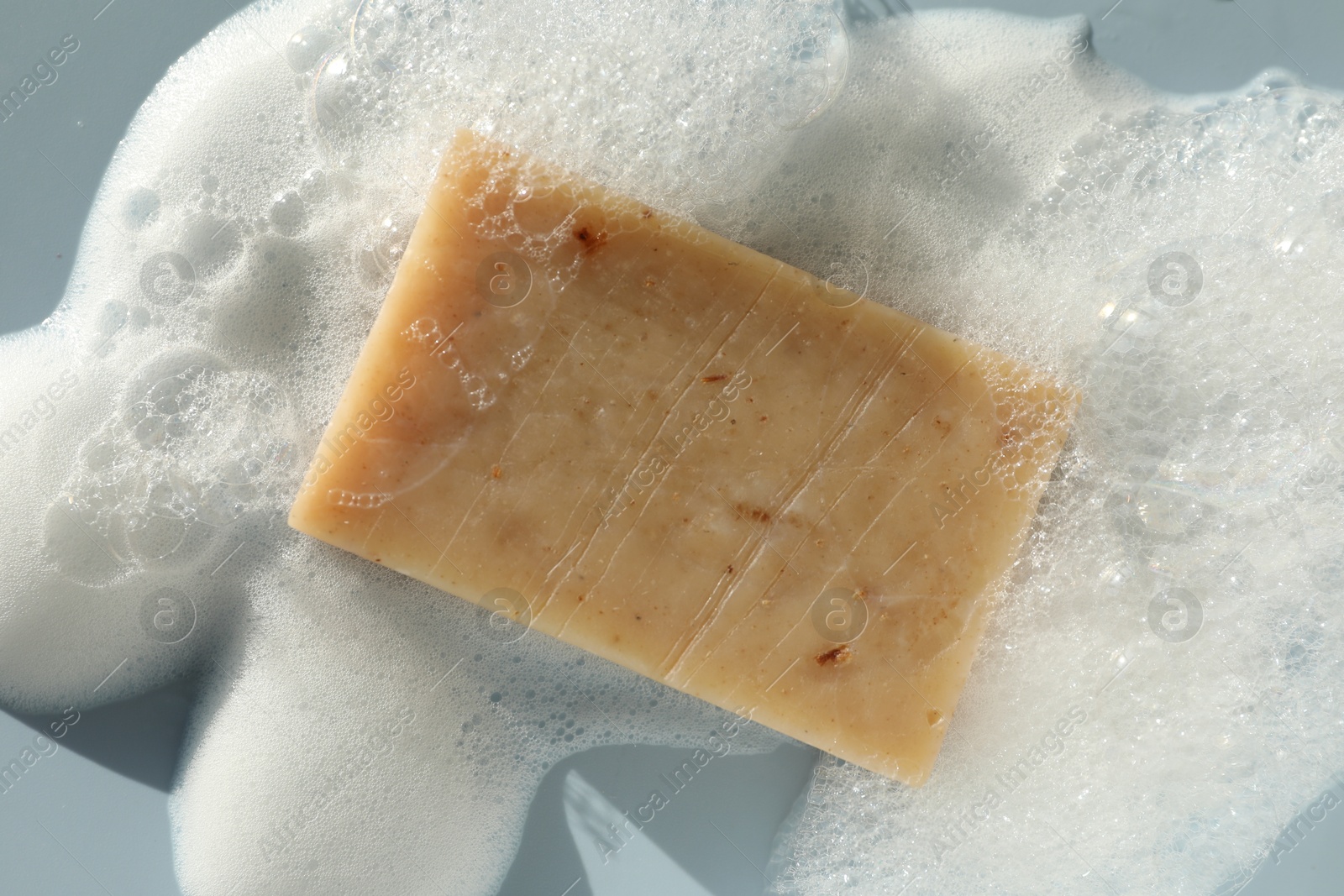 Photo of Soap bar with foam on grayish blue background, top view